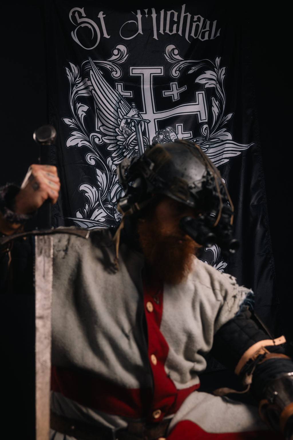 Sir BiggDomm in Opscore helmet with a Saint Michael Flag in the background in a military setting.